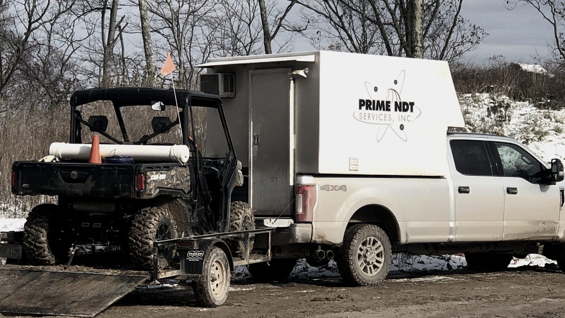 A Prime NDT service truck with a UTV loaded on its trailer at a field site in winter conditions